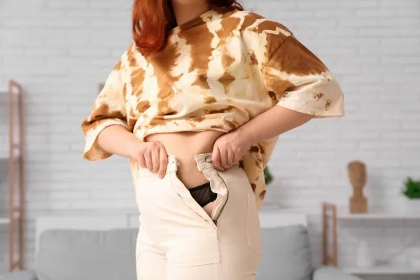 Image of woman trying to do her trousers up after pregnancy weight gain Leicester