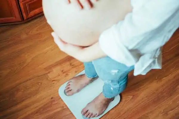 Image of woman weighing herself and experiencing weight gain through pregnancy Leicester